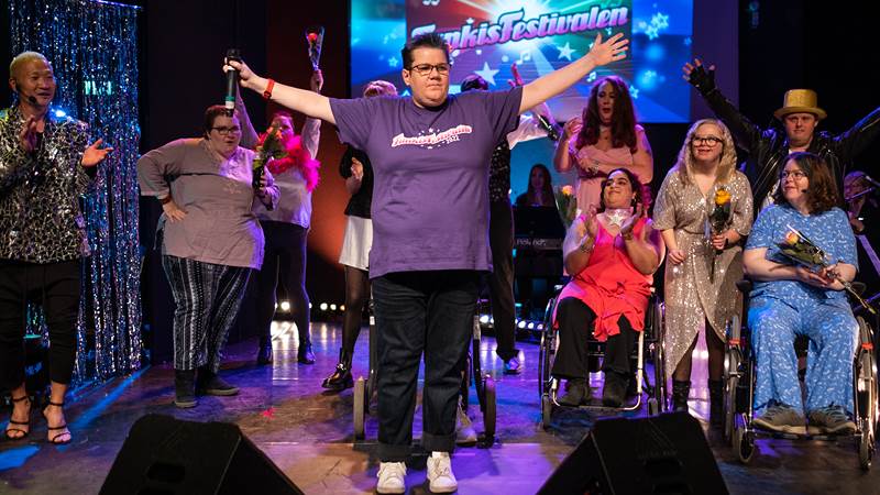 Susanne Eklund vann Funkisfestivalen 2022. Vem vinner i år?  Susanne Eklund står på scen och får beskedet att hon vunnit Funkisfestivalen i Haninge. Övriga tävlande står bakom henne på scen.