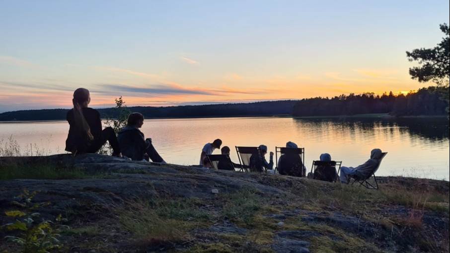 Ungdomar sitter på ett berg och ser ut över en solnedgång på sommarläger