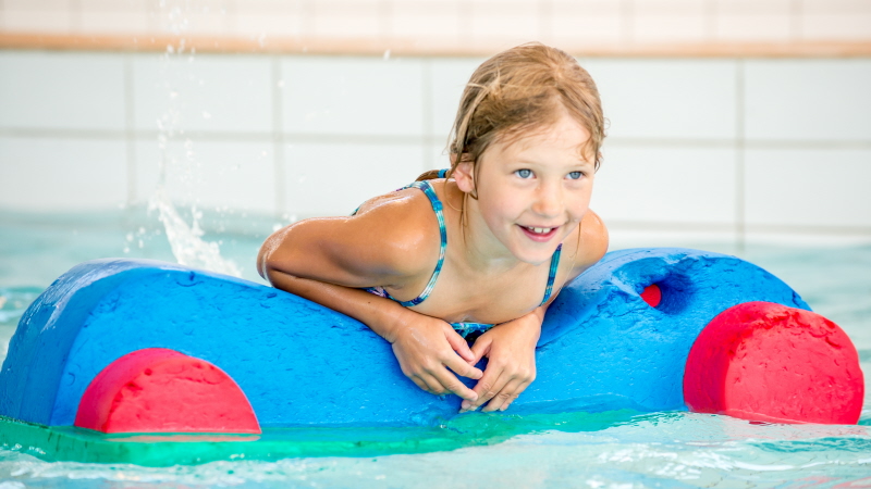 Flicka på flytleksak i en simbassäng.