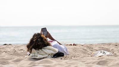 En tjej ligger på stranden och har sin mobiltelefon i handen