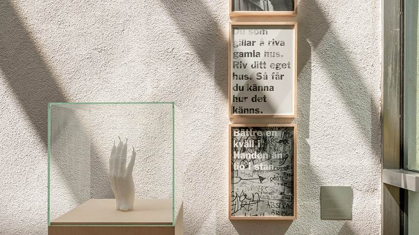 Skulptur av en hand och tre texter uppsatta på väggen.