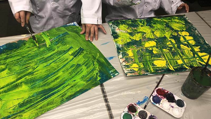 Barnhänder som målar med grön akrylfärg..