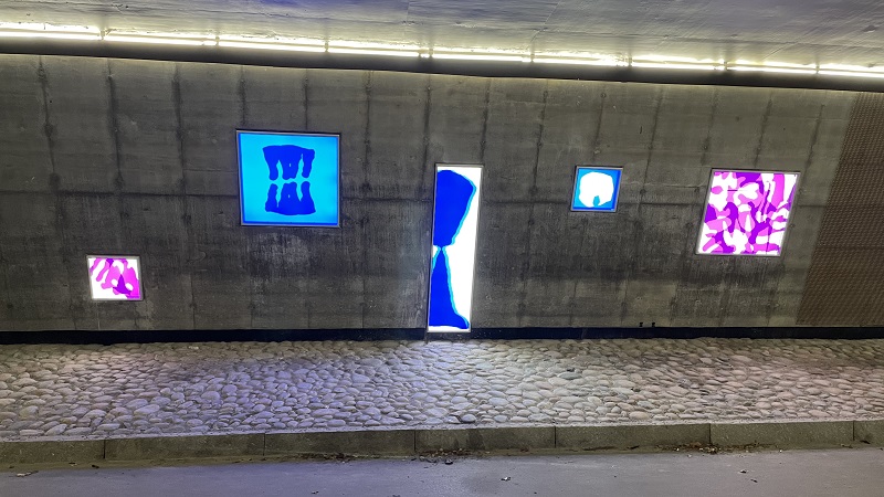 Konst i lila och blått i ljuslådor i gångtunnel