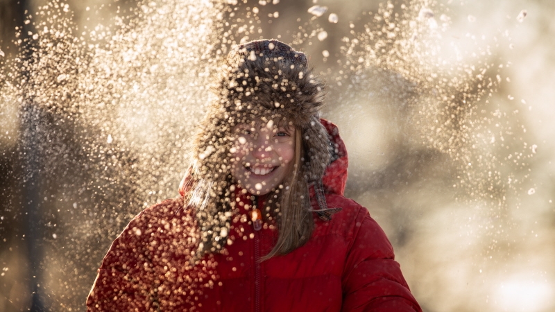 En flicka som står i motljus med snö som faller runt henne