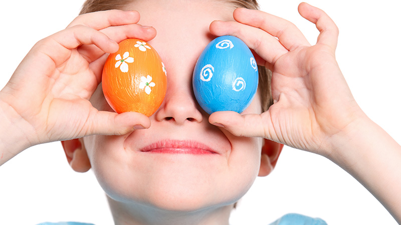 Kille som håller två färgglada ägg framför ögonen.