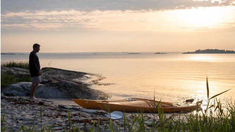 Kajak i solnedgången på Nåttarö.  Person står vid kajak på stranden på Nåttarö