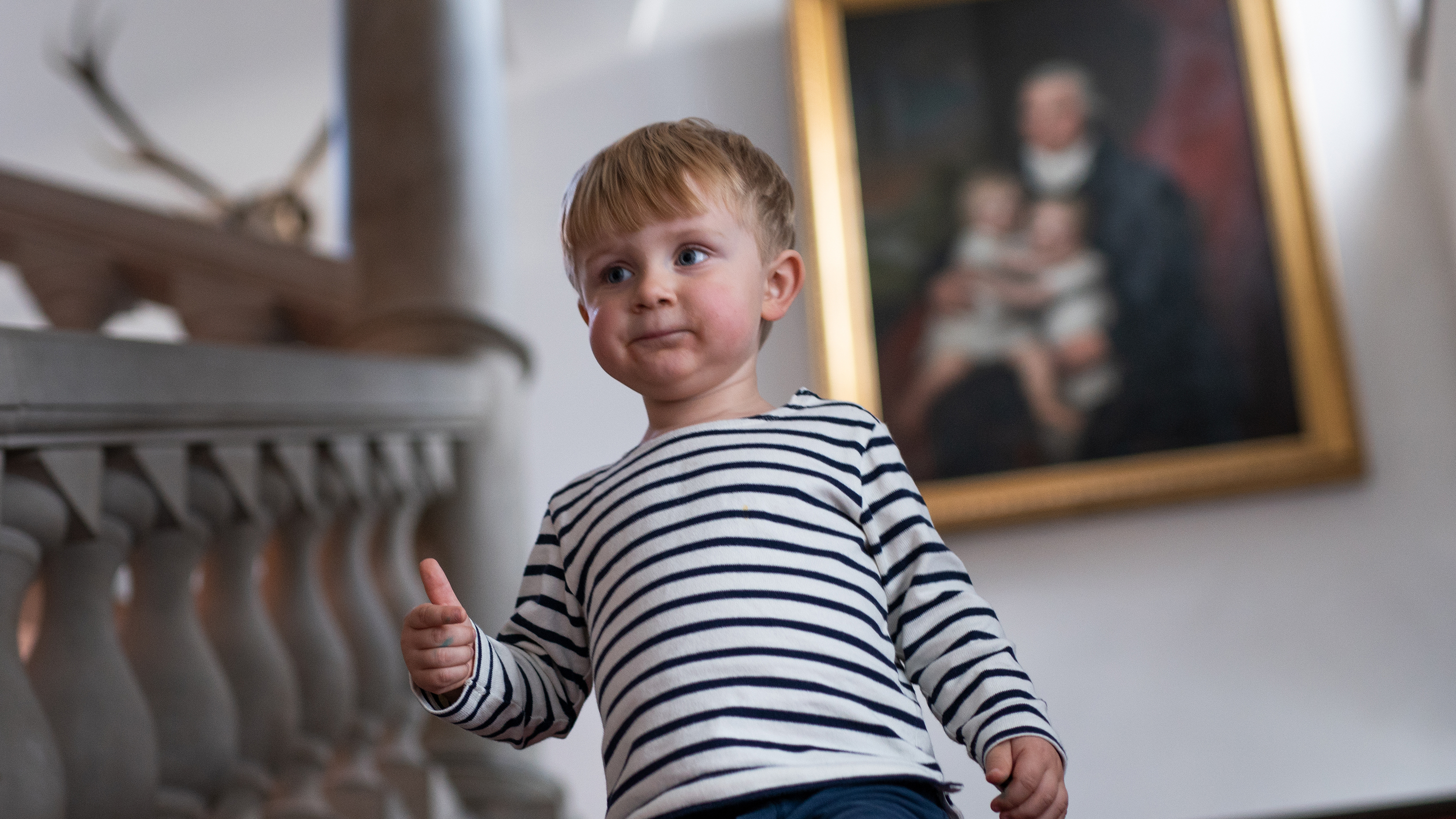 Pojke med ljust hår, ca fyra år gammal går ned för en stentrappa. Bakom honom en oljemålning som föreställer en man med två små barn i knät.