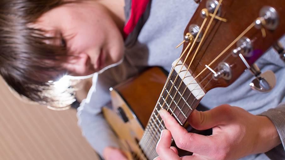 Tonårspojke som spelar gitarr.